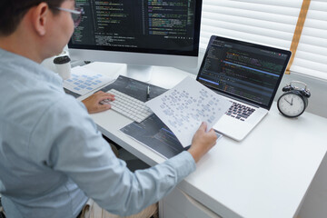 Wall Mural - software development concept, male programmer read data on document while programming on computer