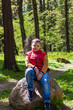 © Alina Lebed - A young man in a sleeveless red jacket is sitting on a huge stone in a pine forest in spring. The magical light from the sun's rays falls behind the boy.