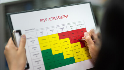 Action of a person is using ballpoint pen to marking on the risk assessment matrix table at 