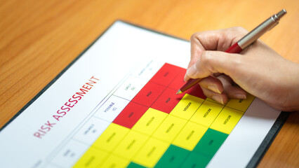 Wall Mural - Action of a person is using ballpoint pen to marking on the risk assessment matrix table at 