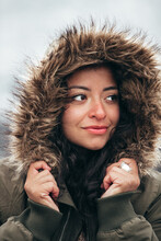 Young Hispanic Woman In Green Fur Parka Jacket In Cold Winter With Blurry Mountain Background