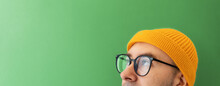 Close Up Face Of Young Man With Glasses And A Hat Looking At The Left Top Side. Banner With Copy Space. The Concept Of Choice, Vision And Searching
