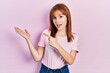 © Krakenimages.com - Redhead young woman wearing casual pink t shirt amazed and smiling to the camera while presenting with hand and pointing with finger.