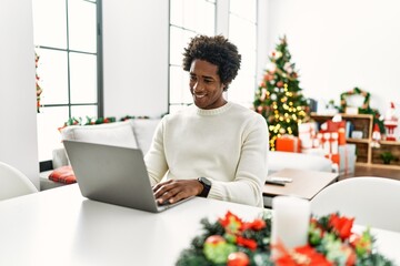 Poster - Young african american man using laptop sitting on the table by christmas tree with a happy and cool smile on face. lucky person.