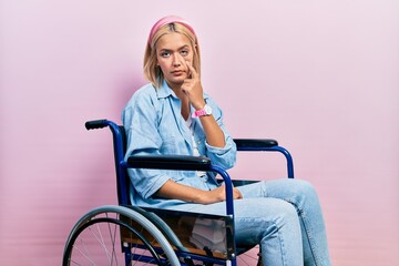 Poster - Beautiful blonde woman sitting on wheelchair pointing to the eye watching you gesture, suspicious expression