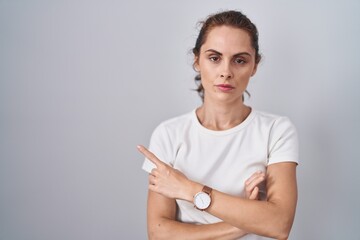 Sticker - Beautiful brunette woman standing over isolated background pointing with hand finger to the side showing advertisement, serious and calm face