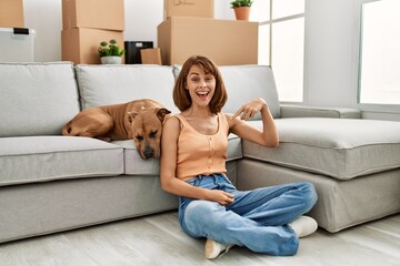 Poster - Young caucasian girl wearing casual clothes sitting on the floor with dog at home pointing finger to one self smiling happy and proud