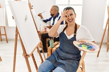 Poster - Young artist woman at art studio smiling happy doing ok sign with hand on eye looking through fingers