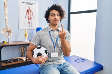 Canvas Print - Hispanic man with curly hair working as football physiotherapist showing middle finger, impolite and rude fuck off expression