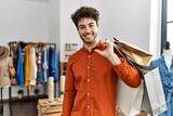 Young hispanic customer man smiling happy holding shopping bags at clothing store.