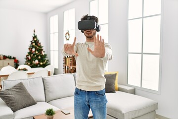 Sticker - Young hispanic man smiling happy using 3d vr glasses at home.