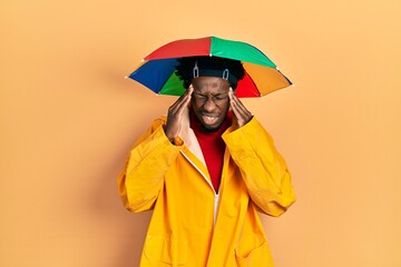 Poster - Young african american man wearing yellow raincoat with hand on head, headache because stress. suffering migraine.