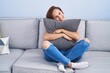 © Krakenimages.com - Young woman hugging cushion sitting on sofa at home