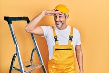 Handsome Middle Age Man With Grey Hair Holding Ladder Very Happy And Smiling Looking Far Away With Hand Over Head. Searching Concept.