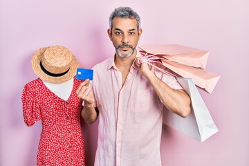 Poster - Handsome middle age man with grey hair holding shopping bags and credit card relaxed with serious expression on face. simple and natural looking at the camera.