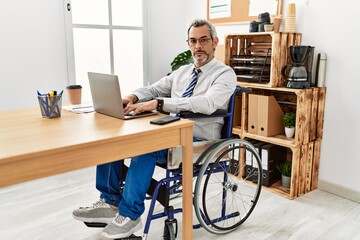 Poster - Middle age hispanic man working at the office sitting on wheelchair relaxed with serious expression on face. simple and natural looking at the camera.