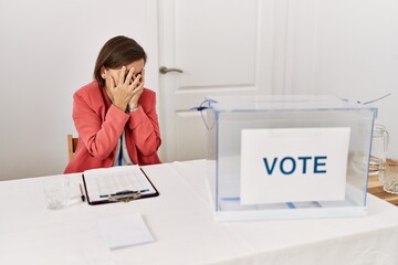 Poster - Beautiful middle age hispanic woman at political election sitting by ballot with sad expression covering face with hands while crying. depression concept.