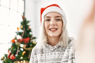 Poster - Young caucasian girl smiling happy wearing christmas hat making selfie by the camera at home.