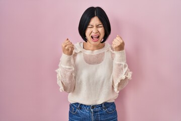 Sticker - Young asian woman standing over pink background excited for success with arms raised and eyes closed celebrating victory smiling. winner concept.