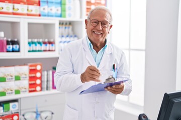 Canvas Print - Senior grey-haired man pharmacist writing on document at pharmacy