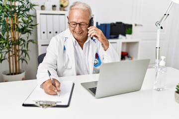 Poster - Senior man wearing doctor uniform talking on the smartphone at clinic