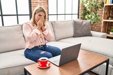 Young Hispanic Woman Using Laptop Sitting On The Sofa At Home Smelling Something Stinky And Disgusting, Intolerable Smell, Holding Breath With Fingers On Nose. Bad Smell