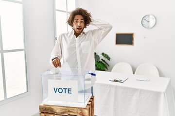 Poster - Young hispanic man voting putting envelop in ballot box crazy and scared with hands on head, afraid and surprised of shock with open mouth