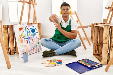 Sticker - Young hispanic man at art studio looking unhappy and angry showing rejection and negative with thumbs down gesture. bad expression.