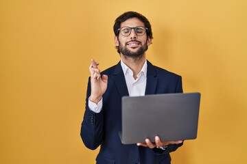 Poster - Handsome latin man working using computer laptop gesturing finger crossed smiling with hope and eyes closed. luck and superstitious concept.