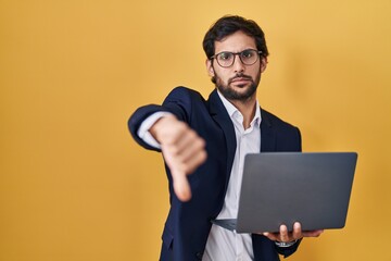 Sticker - Handsome latin man working using computer laptop looking unhappy and angry showing rejection and negative with thumbs down gesture. bad expression.