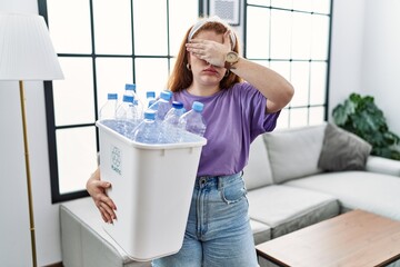 Sticker - Young redhead woman holding recycling wastebasket with plastic bottles covering eyes with hand, looking serious and sad. sightless, hiding and rejection concept