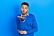 © Krakenimages.com - Young hispanic man with beard wearing casual blue sweater looking at the camera blowing a kiss with hand on air being lovely and sexy. love expression.