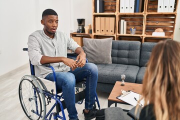 Poster - African american man doing therapy sitting on wheelchair afraid and shocked with surprise expression, fear and excited face.