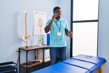 Sticker - Young african american man physiotherapist talking on the smartphone and drinking coffee al rehab clinic