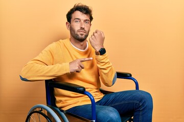 Poster - Handsome man with beard sitting on wheelchair in hurry pointing to watch time, impatience, looking at the camera with relaxed expression