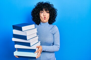 Sticker - Young middle east woman holding a pile of books making fish face with mouth and squinting eyes, crazy and comical.