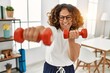 © Krakenimages.com - Middle age hispanic woman smiling confident training using dumbbells at home