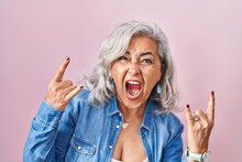 Middle Age Woman With Grey Hair Standing Over Pink Background Shouting With Crazy Expression Doing Rock Symbol With Hands Up. Music Star. Heavy Music Concept.