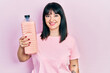 © Krakenimages.com - Young hispanic woman holding detergent bottle looking positive and happy standing and smiling with a confident smile showing teeth