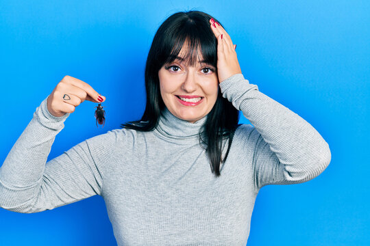 Young hispanic woman holding cockroach stressed and frustrated with hand on head, surprised and angry face