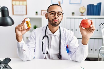 Sticker - African american doctor man holding prescription pills and fresh apple looking at the camera blowing a kiss being lovely and sexy. love expression.