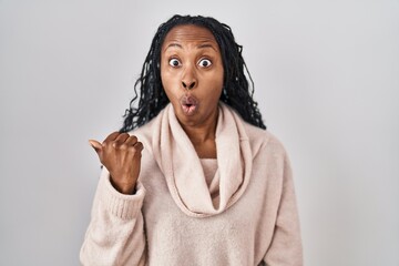 Sticker - African woman standing over white background surprised pointing with hand finger to the side, open mouth amazed expression.