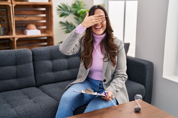 Sticker - Young brunette woman working at consultation office smiling and laughing with hand on face covering eyes for surprise. blind concept.