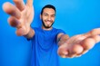 © Krakenimages.com - Hispanic man with beard wearing casual blue t shirt looking at the camera smiling with open arms for hug. cheerful expression embracing happiness.
