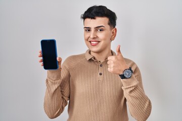 Canvas Print - Non binary person holding smartphone showing blank screen smiling happy and positive, thumb up doing excellent and approval sign