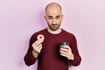 Poster - Young bald man drinking coffee and eating pastry depressed and worry for distress, crying angry and afraid. sad expression.