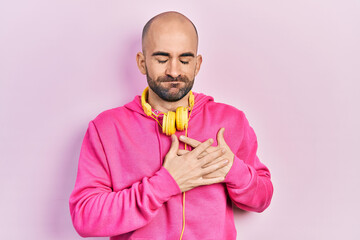 Canvas Print - Young bald man wearing gym clothes and using headphones smiling with hands on chest with closed eyes and grateful gesture on face. health concept.