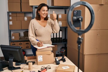 Wall Mural - Middle age hispanic woman working at small business ecommerce doing online tutorial smiling happy and positive, thumb up doing excellent and approval sign