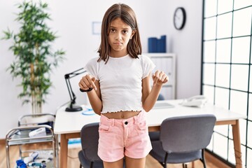 Wall Mural - Young hispanic girl standing at pediatrician clinic pointing down looking sad and upset, indicating direction with fingers, unhappy and depressed.