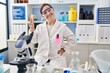 © Krakenimages.com - Hispanic girl with down syndrome working at scientist laboratory smiling looking to the camera showing fingers doing victory sign. number two.